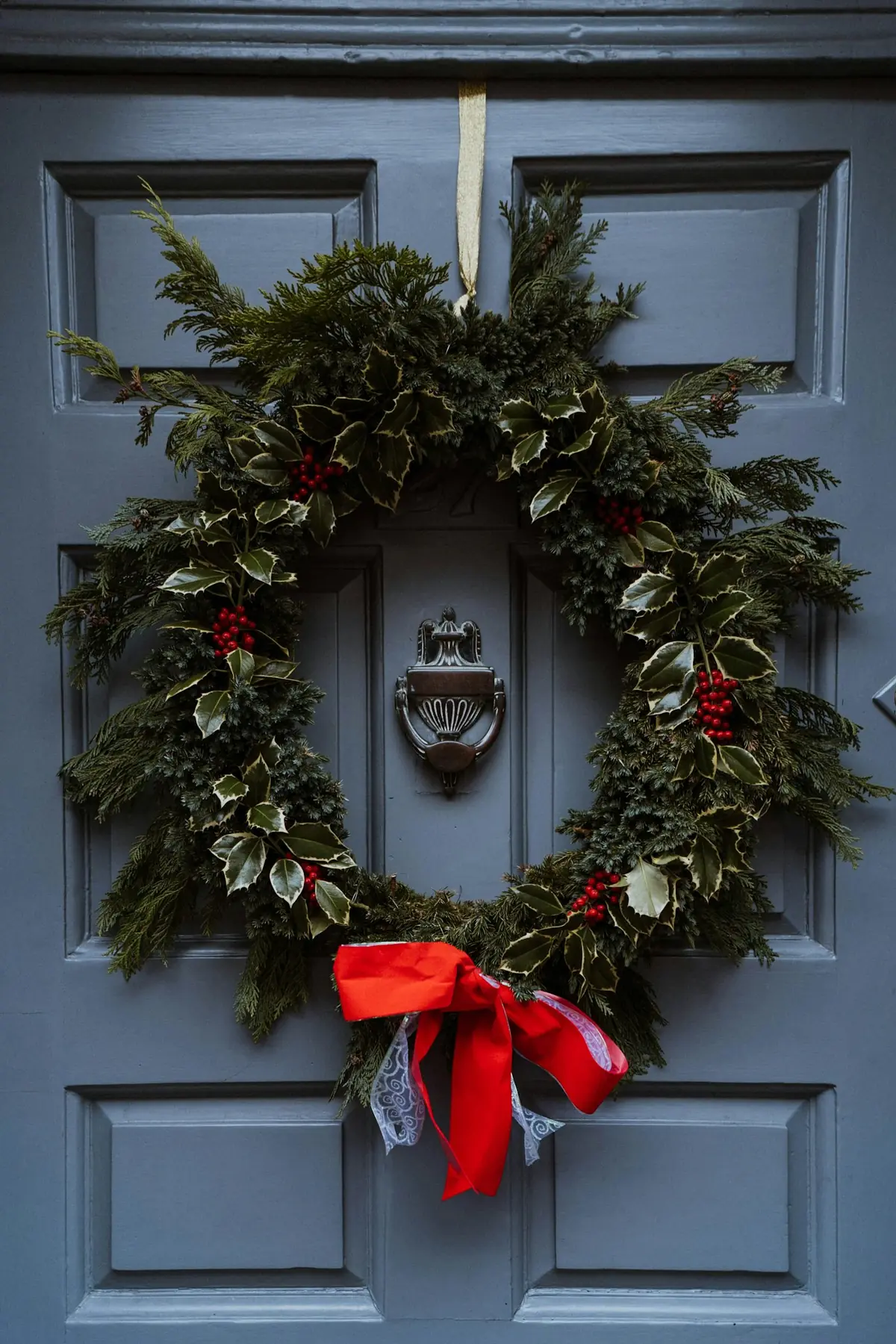 An evergreen wreath with a red bow on a slate-blue front door