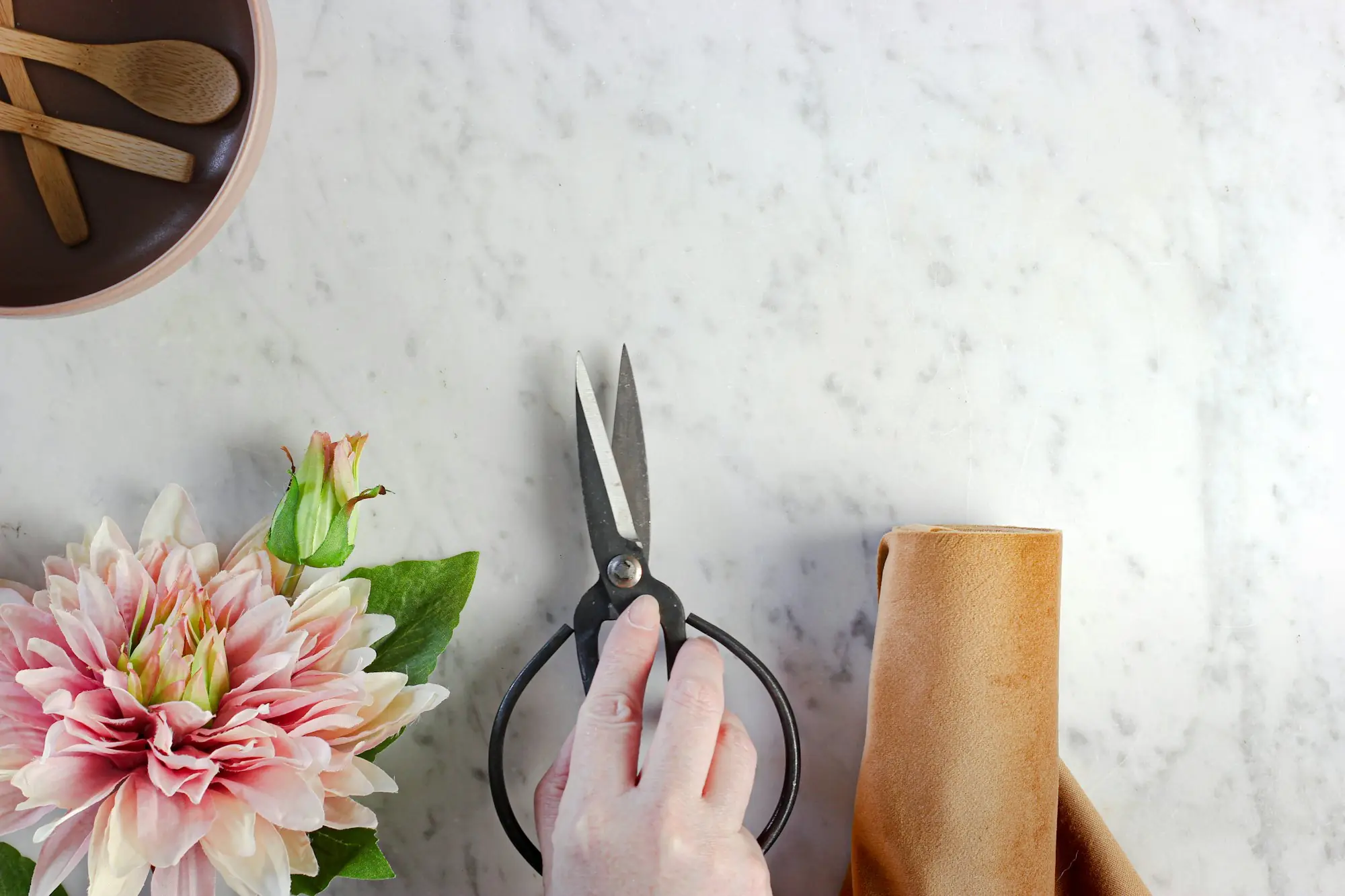 A hand cutting stems beside a pink dahlia on a marble bench