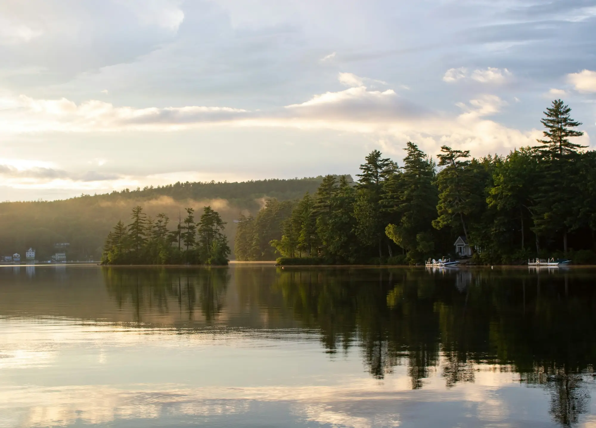 A still lake reflecting dark pines and a pale sky
