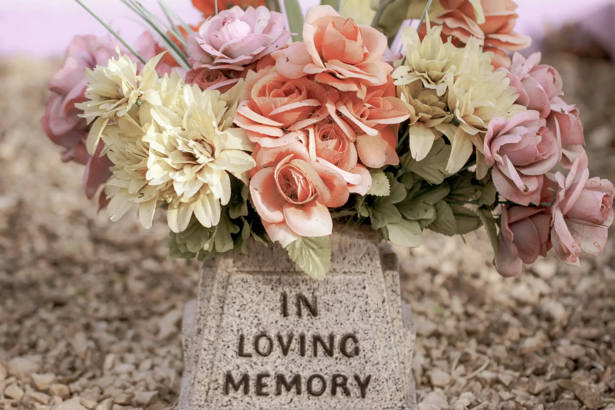 Peach and cream flowers resting on a stone marked In Loving Memory